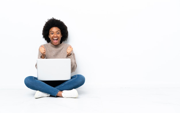 Giovane donna afro-americana con un laptop seduto sul pavimento isolato