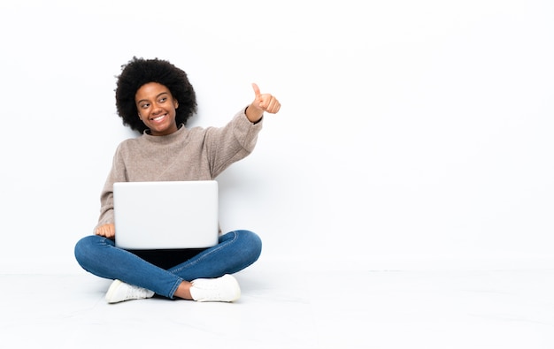 Giovane donna afro-americana con un laptop seduto sul pavimento isolato