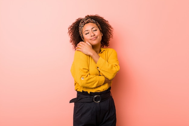 Giovane donna afro-americana contro un abbracci rosa, sorridente spensierato e felice.