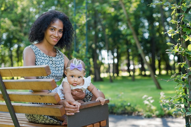 Giovane donna afro-americana e sua figlia sorridente seduto sulla panchina nel parco estivo.