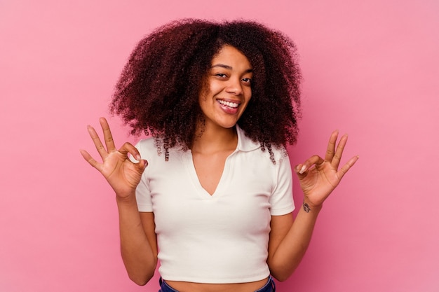 Giovane donna afro-americana isolata su rosa allegro e fiducioso che mostra gesto giusto.