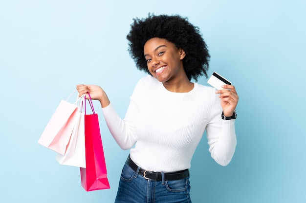 Giovane donna afro-americana isolata su sfondo blu tenendo le borse della spesa e una carta di credito