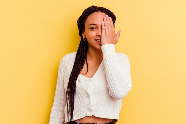 Giovane donna afro-americana isolata su sfondo giallo divertendosi che copre metà del viso con il palmo.