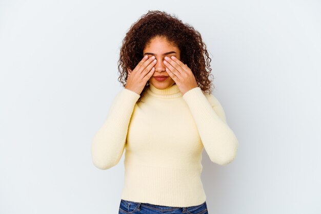 Giovane donna afro-americana isolata sul muro bianco paura che copre gli occhi con le mani.