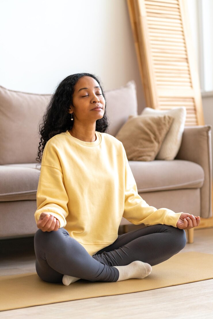 Foto giovane donna afro-americana seduta in postura di yoga al loto sul tappetino mentre medita verticalmente