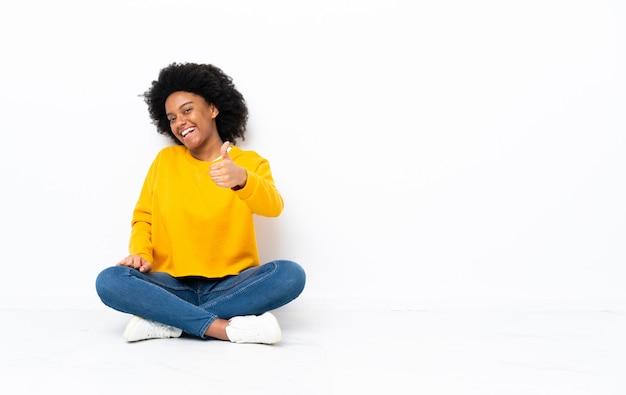 Giovane donna afro-americana seduta sul pavimento con il pollice in alto perché è successo qualcosa di buono