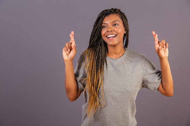 Giovane donna afro brasiliana con le dita incrociate torcendosi desiderando la lotteria della fortuna