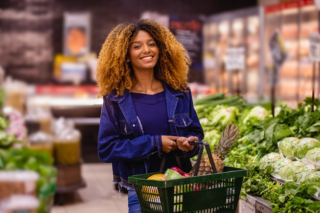 Giovane donna afro che compra verdure al supermercato.