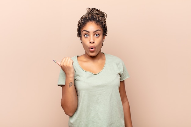 Giovane donna afro che guarda stupita incredula, indicando un oggetto sul lato e dicendo wow, incredibile