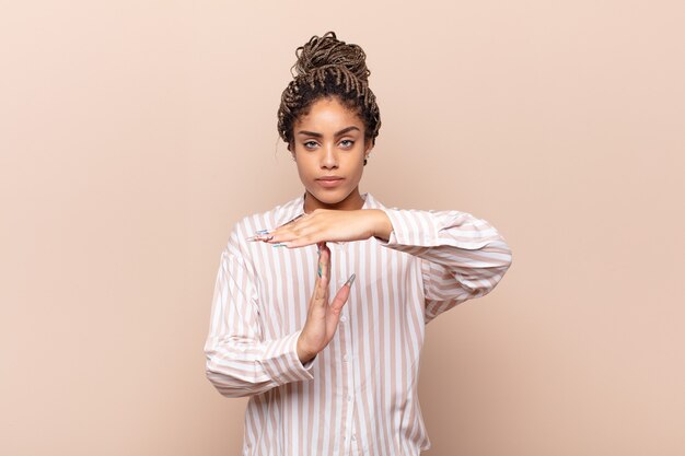 Giovane donna afro che sembra seria, severa, arrabbiata e scontenta, facendo segno di time out