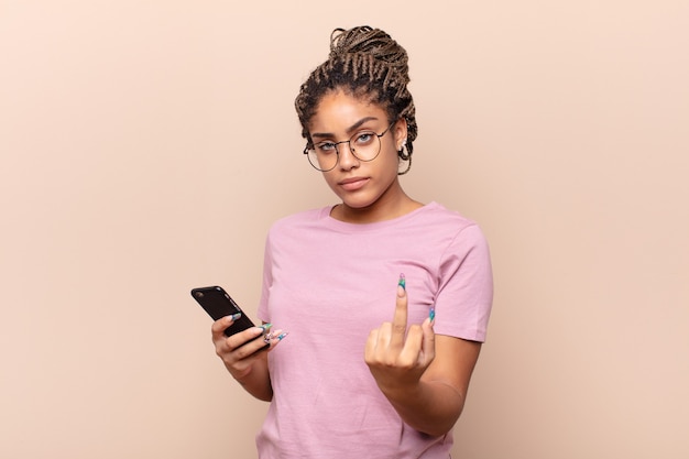 Giovane donna afro che si sente arrabbiata, infastidita, ribelle e aggressiva, lanciando il dito medio, contrattaccando. concetto di smartphone