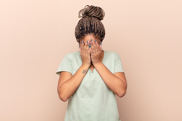 Giovane donna afro che si sente triste, frustrata, nervosa e depressa, coprendosi il viso con entrambe le mani, piangendo