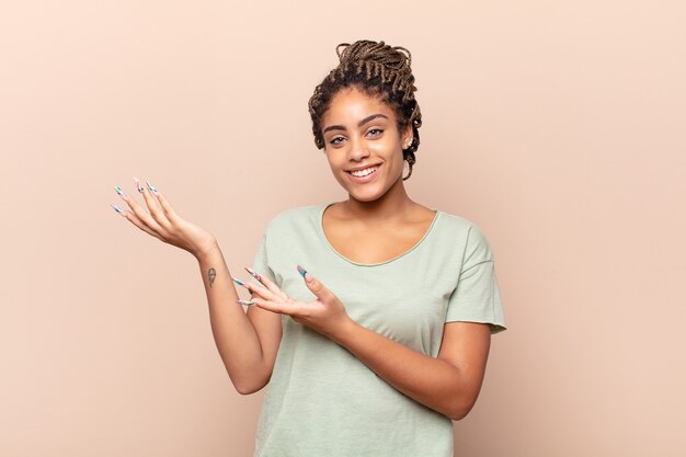 Giovane donna afro che sorride con orgoglio e sicurezza, sentendosi felice e soddisfatta e mostrando un concetto sullo spazio della copia