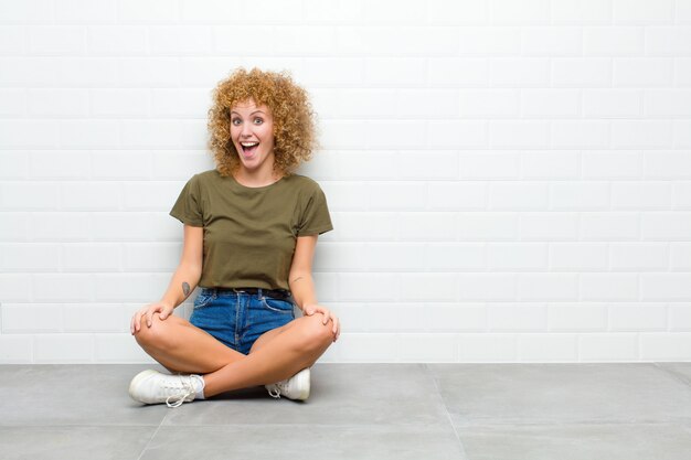 Giovane donna afro con un sorriso grande, amichevole, spensierato, dall'aspetto positivo, rilassato e felice, agghiacciante seduto su un piano