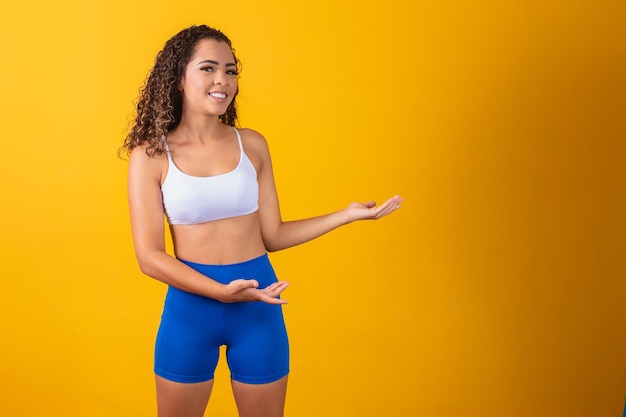 Giovane donna afro in attrezzatura da palestra che punta al lato con spazio per il testo.