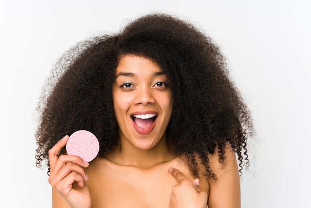 Giovane donna afro in possesso di un disco facciale sorpreso indicando se stessa, sorridendo ampiamente