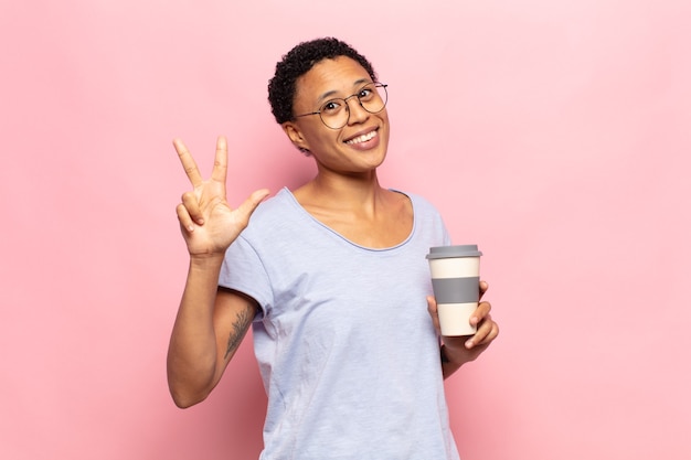 Giovane donna afro nera che sorride e sembra amichevole, mostrando il numero tre o il terzo con la mano in avanti, conto alla rovescia