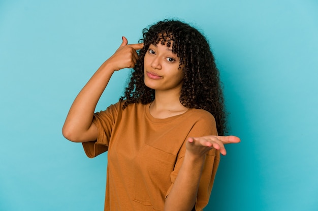 Giovane donna afroamericana afro azienda isolata e mostrando un prodotto a portata di mano.