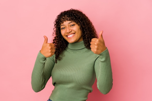 Giovane donna afroamericana afro isolata sorridendo e alzando il pollice