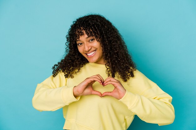 Giovane donna afroamericana afro isolata sorridente e mostrando una forma di cuore con le mani.