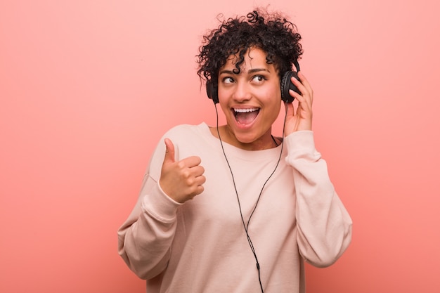 Giovane donna afroamericana che ascolta la musica che sorride e che alza pollice in su