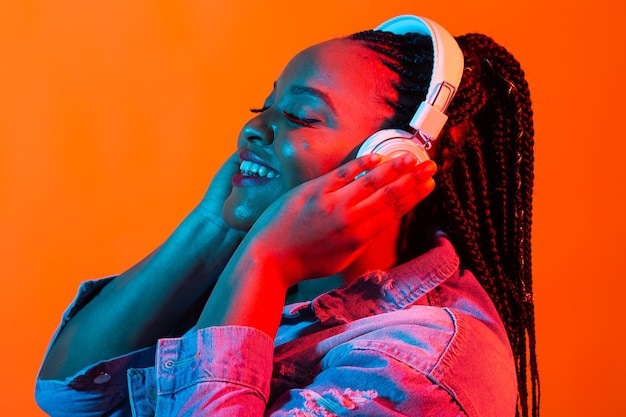 Giovane donna afroamericana che ascolta la musica in linea ballando e cantando con le cuffie, neon