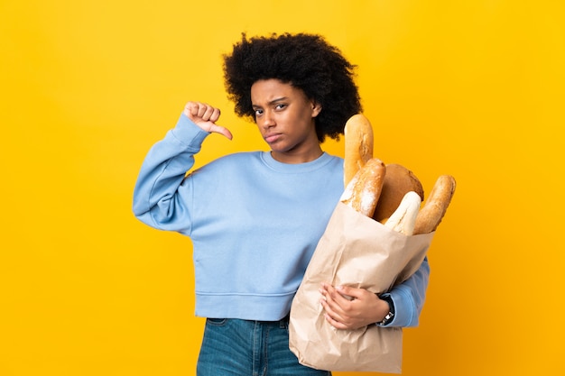 Giovane donna afroamericana che compra qualcosa di pane sulla parete gialla fiera e soddisfatta di sé