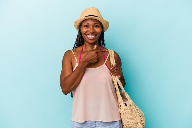 Giovane donna afroamericana che indossa abiti estivi isolati su sfondo blu sorridendo e indicando da parte, mostrando qualcosa in uno spazio vuoto.