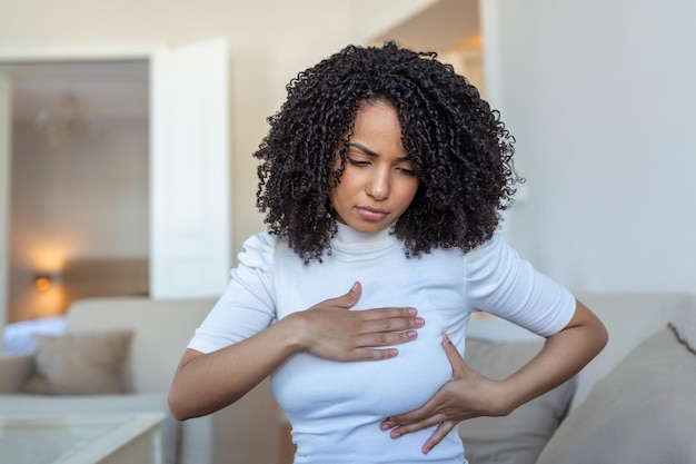 Giovane donna afroamericana che palpa il suo seno da sola che si preoccupa del cancro al seno assistenza sanitaria e concetto di cancro al seno