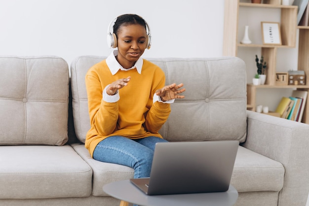Giovane donna afroamericana che parla in videochiamata in soggiorno a casa, concetto di apprendimento a distanza da casa.