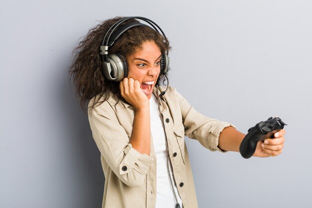 Giovane donna afroamericana che per mezzo delle cuffie e del controller di gioco