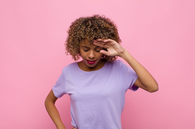 Giovane donna afroamericana che sembra stressata, stanca e frustrata, asciugandosi il sudore dalla fronte, sentendosi senza speranza ed esausta contro il muro rosa