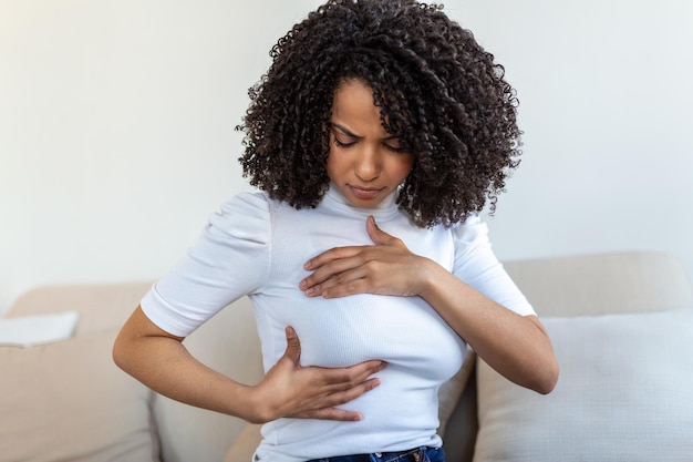 Giovane donna afroamericana che si palpa il seno da sola che si preoccupa per il cancro al seno Concetto di assistenza sanitaria e cancro al seno