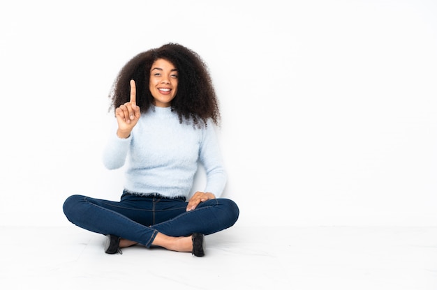 Giovane donna afroamericana che si siede sul pavimento che mostra e che solleva un dito