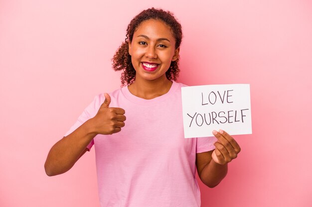 Giovane donna afroamericana che tiene cartello di amore te stesso isolato su sfondo rosa