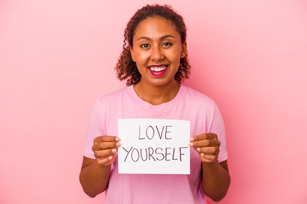 Giovane donna afroamericana che tiene cartello di amore te stesso isolato su sfondo rosa