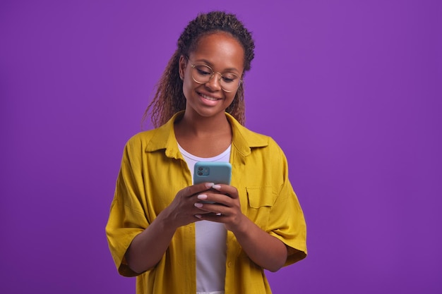 Giovane donna afroamericana che tiene il telefono e sta in chat in studio lilla