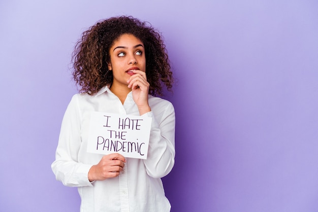 Giovane donna afroamericana che tiene io odio il cartello pandemico isolato sul muro viola rilassato pensando a qualcosa guardando uno spazio di copia.