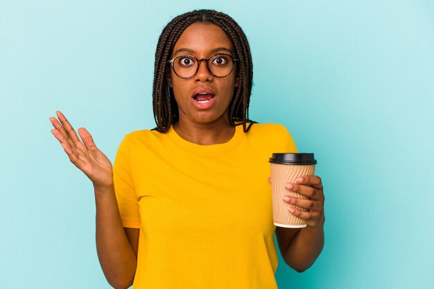 Giovane donna afroamericana che tiene un caffè da asporto isolato su sfondo blu sorpreso e scioccato.