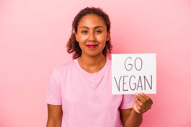 Giovane donna afroamericana che tiene un cartello vegano isolato su sfondo rosa