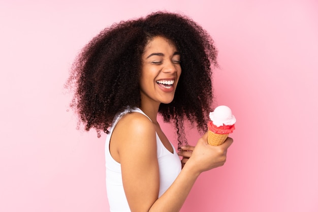 Giovane donna afroamericana che tiene un gelato della cornetta isolato sul colore rosa