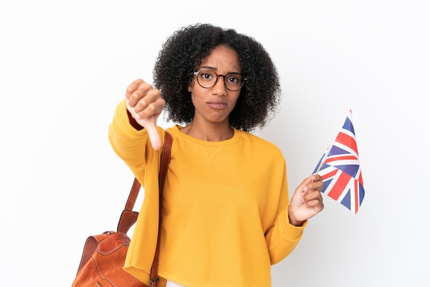 Giovane donna afroamericana che tiene una bandiera del Regno Unito isolata su fondo bianco che mostra il pollice verso il basso con espressione negativa