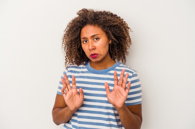 Giovane donna afroamericana con capelli ricci isolati su fondo bianco che rifiuta qualcuno che mostra un gesto di disgusto.