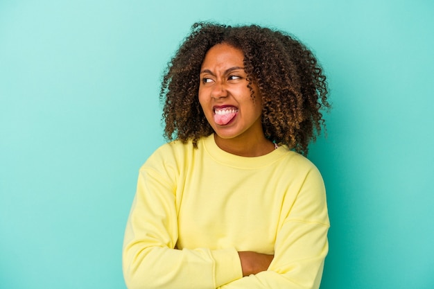 Giovane donna afroamericana con capelli ricci isolati su fondo blu divertente e amichevole che attacca fuori la lingua.