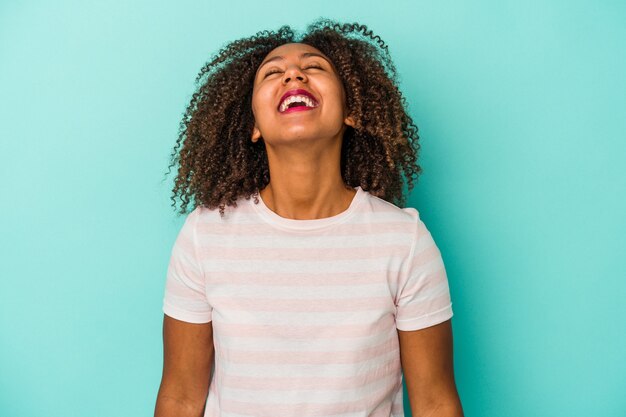 Giovane donna afroamericana con capelli ricci isolati su sfondo blu risata rilassata e felice, collo allungato che mostra i denti.