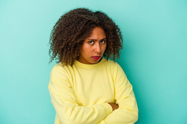 Giovane donna afroamericana con i capelli ricci isolato su sfondo blu sospettoso, incerto, esaminandoti.