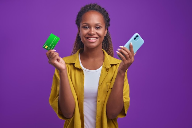 Giovane donna afroamericana con telefono e carta di credito si trova in studio