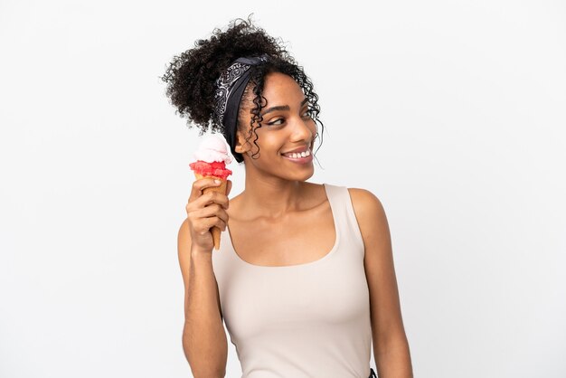 Giovane donna afroamericana con un gelato della cornetta isolato su fondo bianco che guarda side