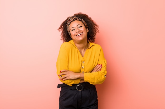 Giovane donna afroamericana contro una parete rosa che ride e che si diverte.