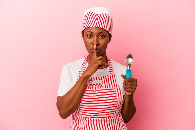 Giovane donna afroamericana del gelatiere che tiene la paletta isolata su sfondo rosa mantenendo un segreto o chiedendo silenzio.